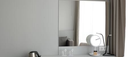 Una habitación moderna y minimalista con un escritorio blanco, una silla, un espejo grande y una mesita de noche con lámpara.
