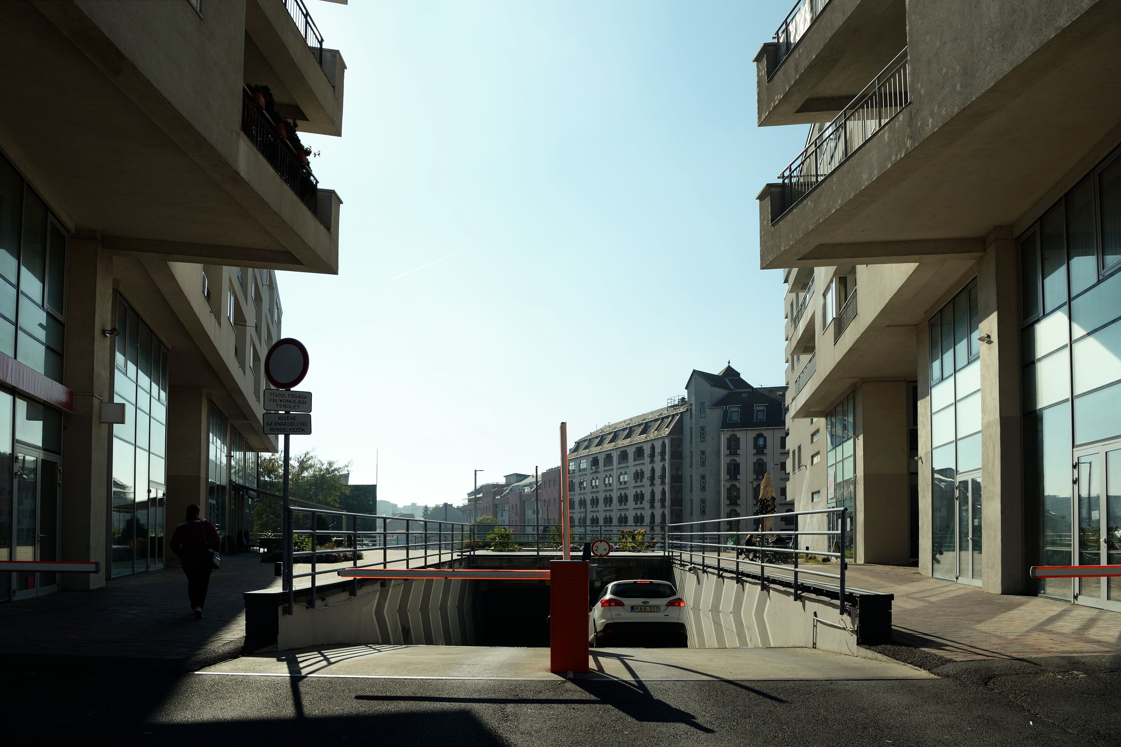 Una passerella pedonale con l'imbocco di un tunnel stradale, edifici moderni e cielo sereno.