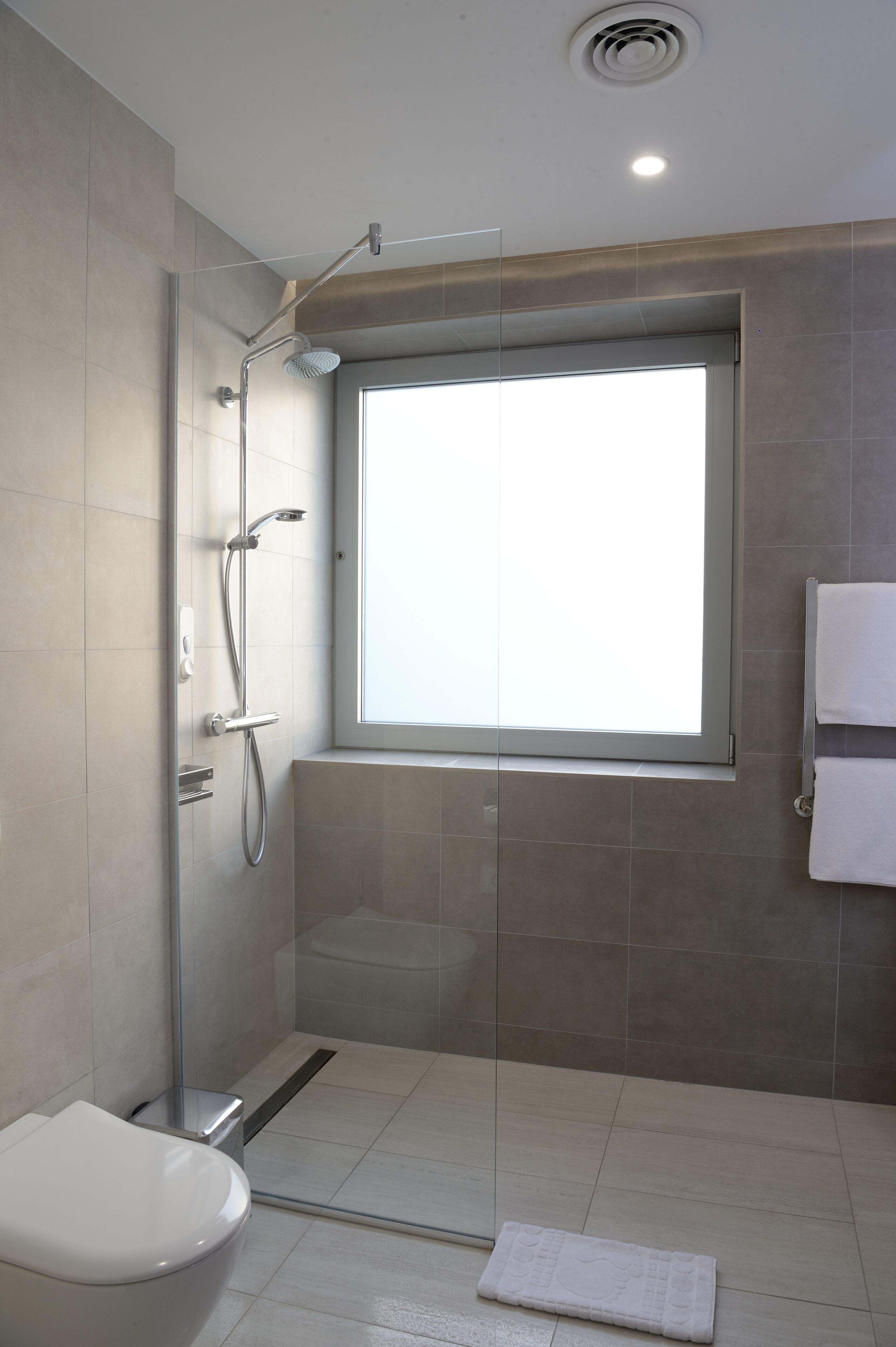 A modern bathroom with a glass shower enclosure, a toilet, and a window providing natural light.