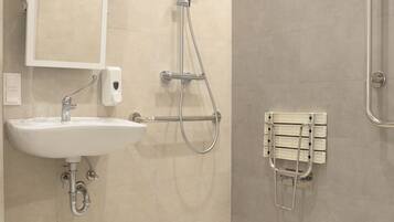A modern bathroom with a sink, mirror, shower, and handrails.