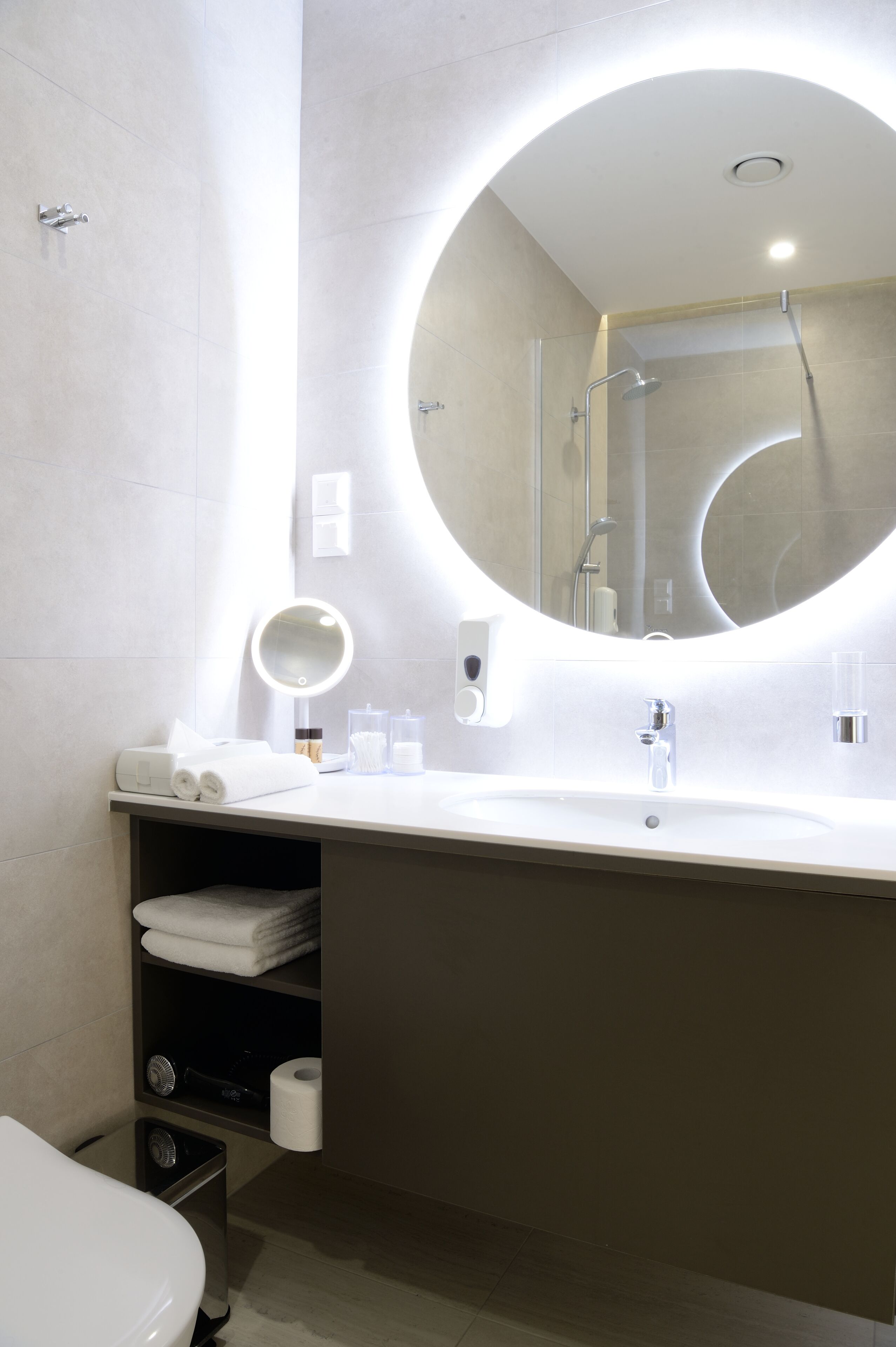 A modern bathroom with a round mirror, a sink, and a toilet.