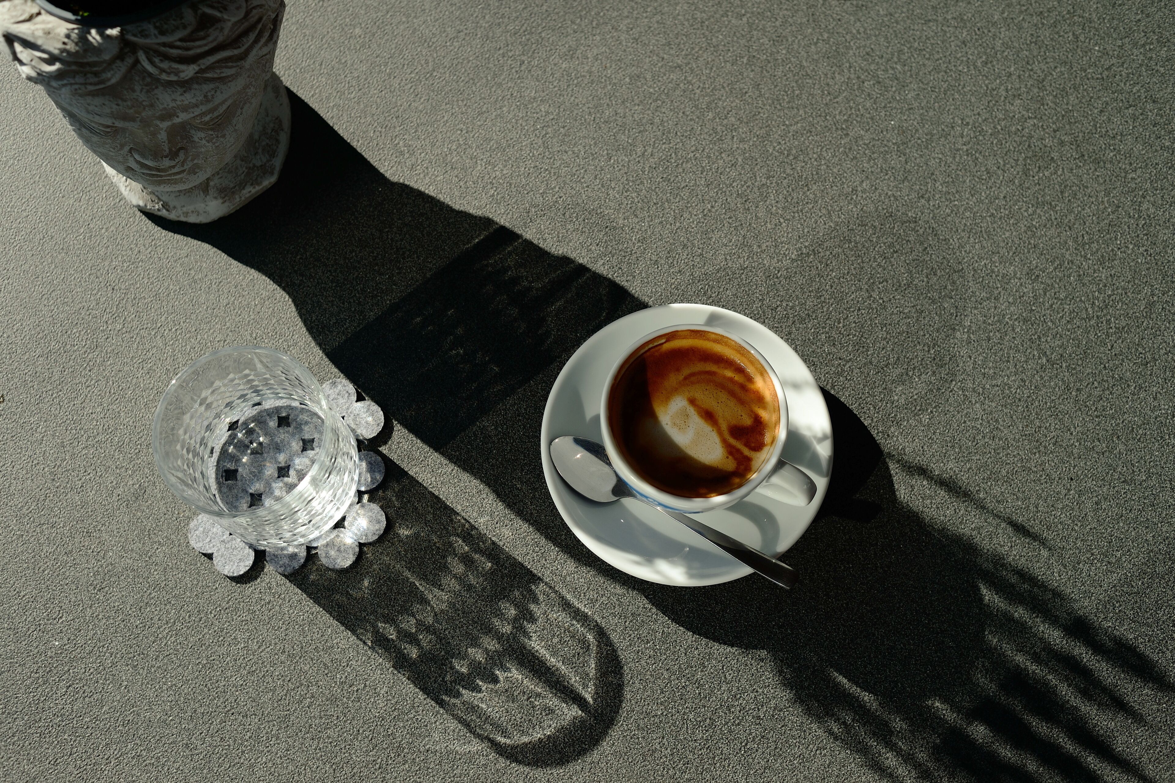 Een kop koffie op een schotel, met een lepeltje, naast een helder glas met rietje.