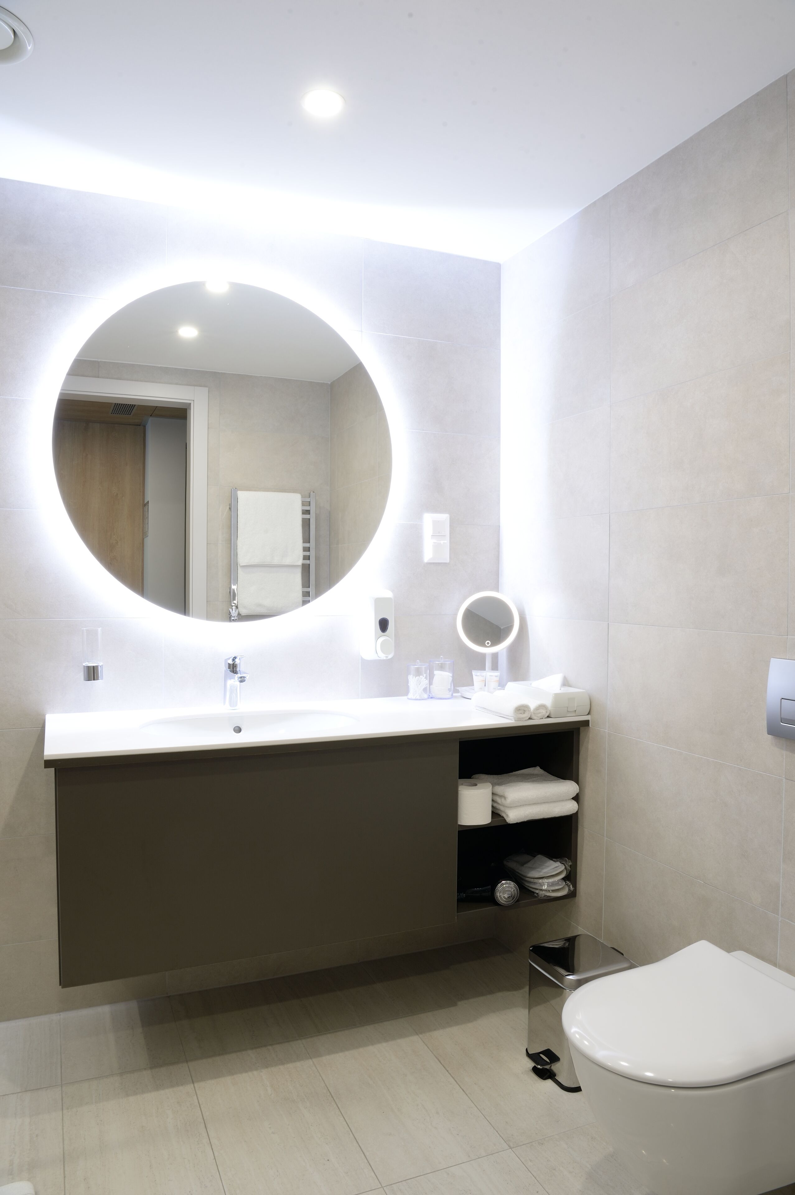 A modern bathroom with a round mirror, a sink, a toilet, and a towel rack.