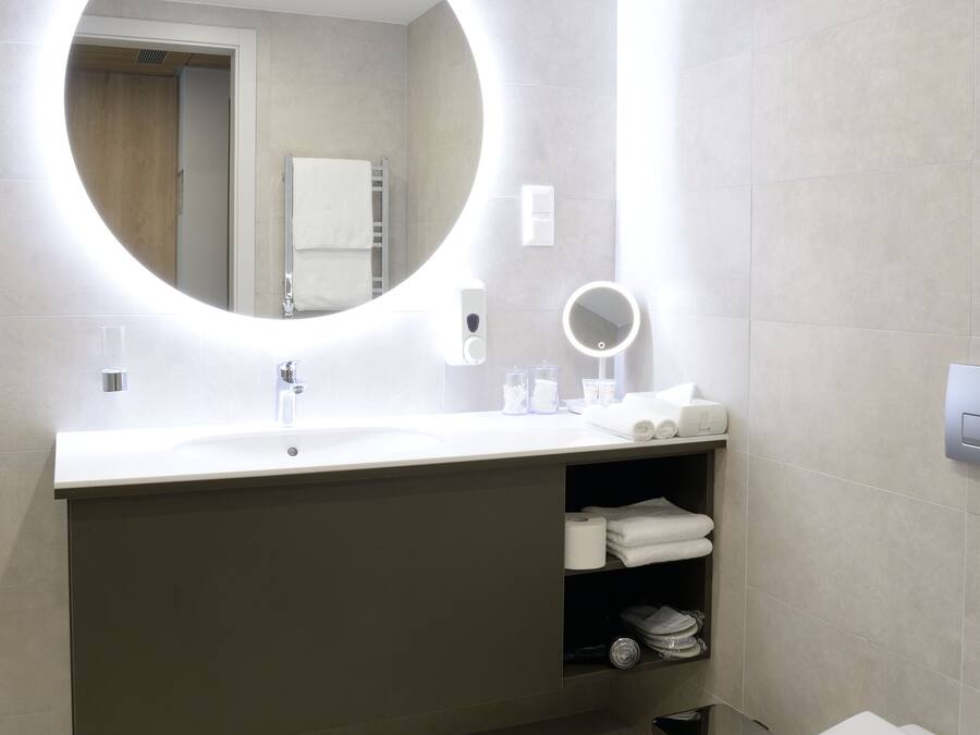 A modern bathroom with a round mirror, a sink, a toilet, and a towel rack.