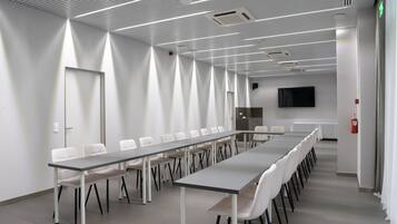 Un salón de conferencias con una larga mesa y sillas, paredes blancas y un televisor de pantalla plana en la pared.