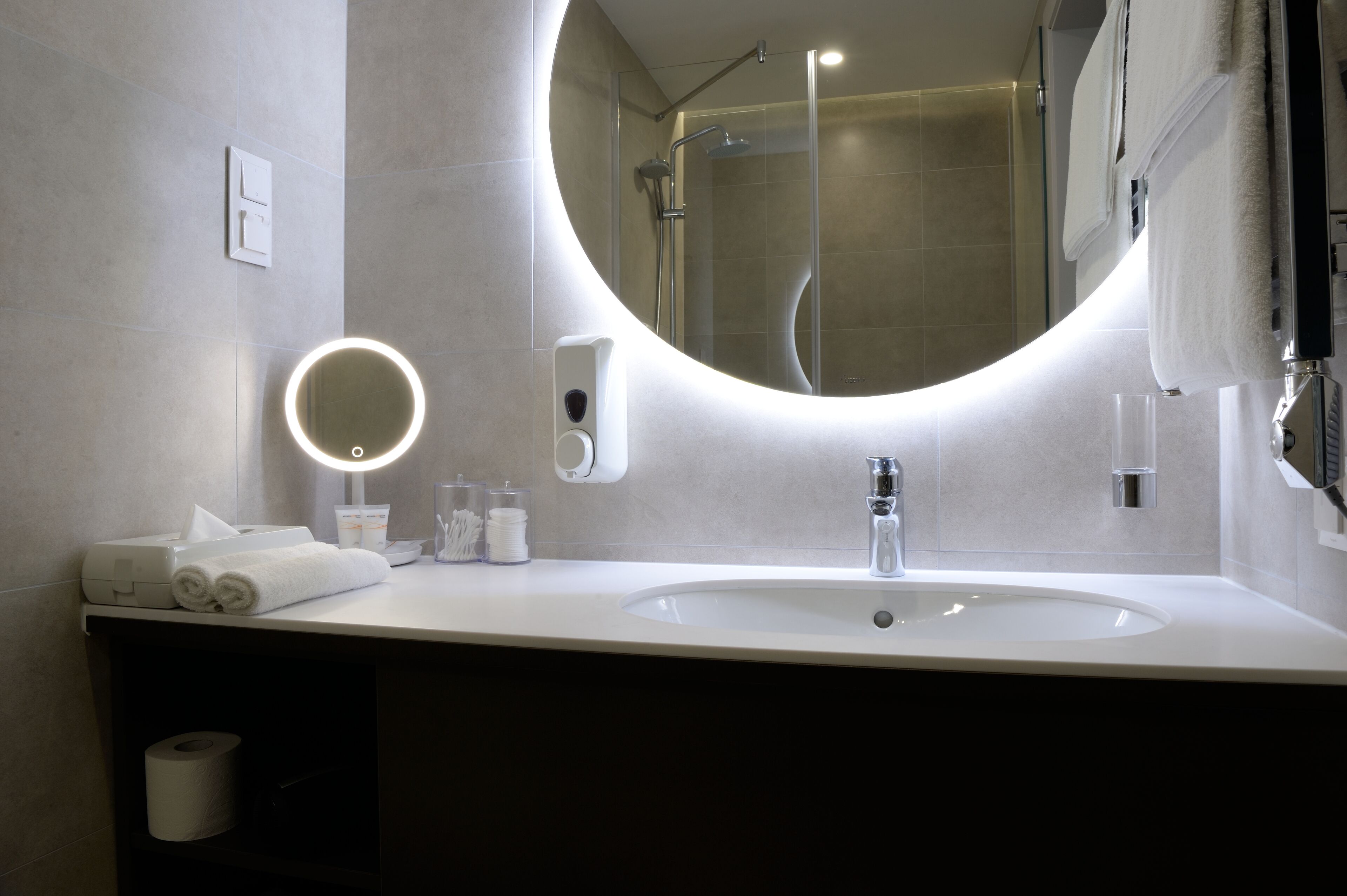 Un baño moderno con un espejo redondo, un lavabo y una ducha.