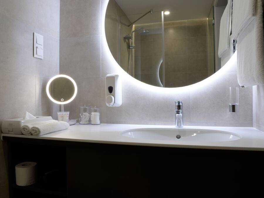 Un baño moderno con un espejo redondo, un lavabo y una ducha.