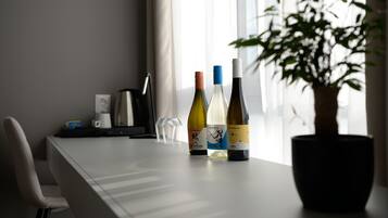 A table with three wine bottles, a coffee maker, and a potted plant in a room with a window.