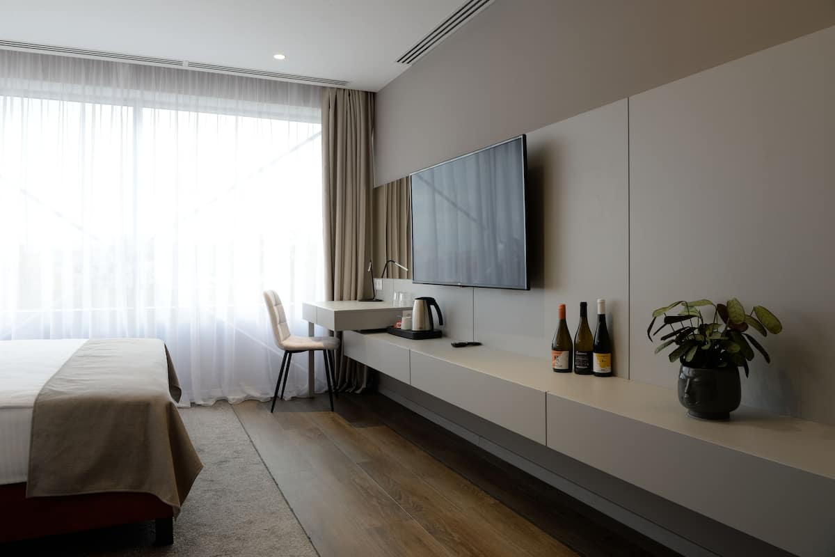 A modern hotel room with a bed, a desk, a flat-screen TV, a coffee maker, and a potted plant.