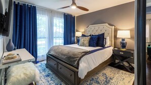 A bedroom with a bed, a ceiling fan, a desk with a lamp, and a view of the outdoors. - Modern Home with a Firepit, Heated Pool & Spa (Dallas)