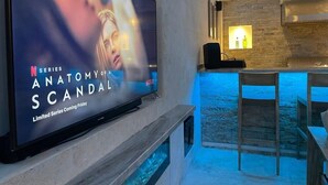 A modern interior with a flat-screen TV displaying a Netflix series, a stone wall, a bar area, and a seating space.