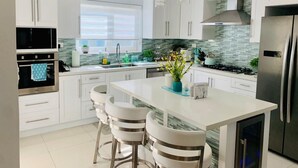 A modern kitchen with white cabinets, a central island with bar stools, stainless steel appliances, and pendant lighting.