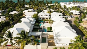 A resort with multiple white-roofed buildings, a swimming pool, and palm trees.