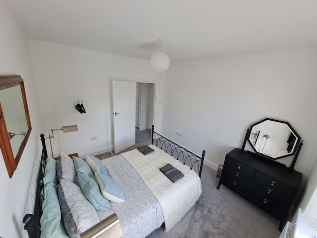 A bedroom with a bed, a dresser, a mirror, and a door leading to another room.
