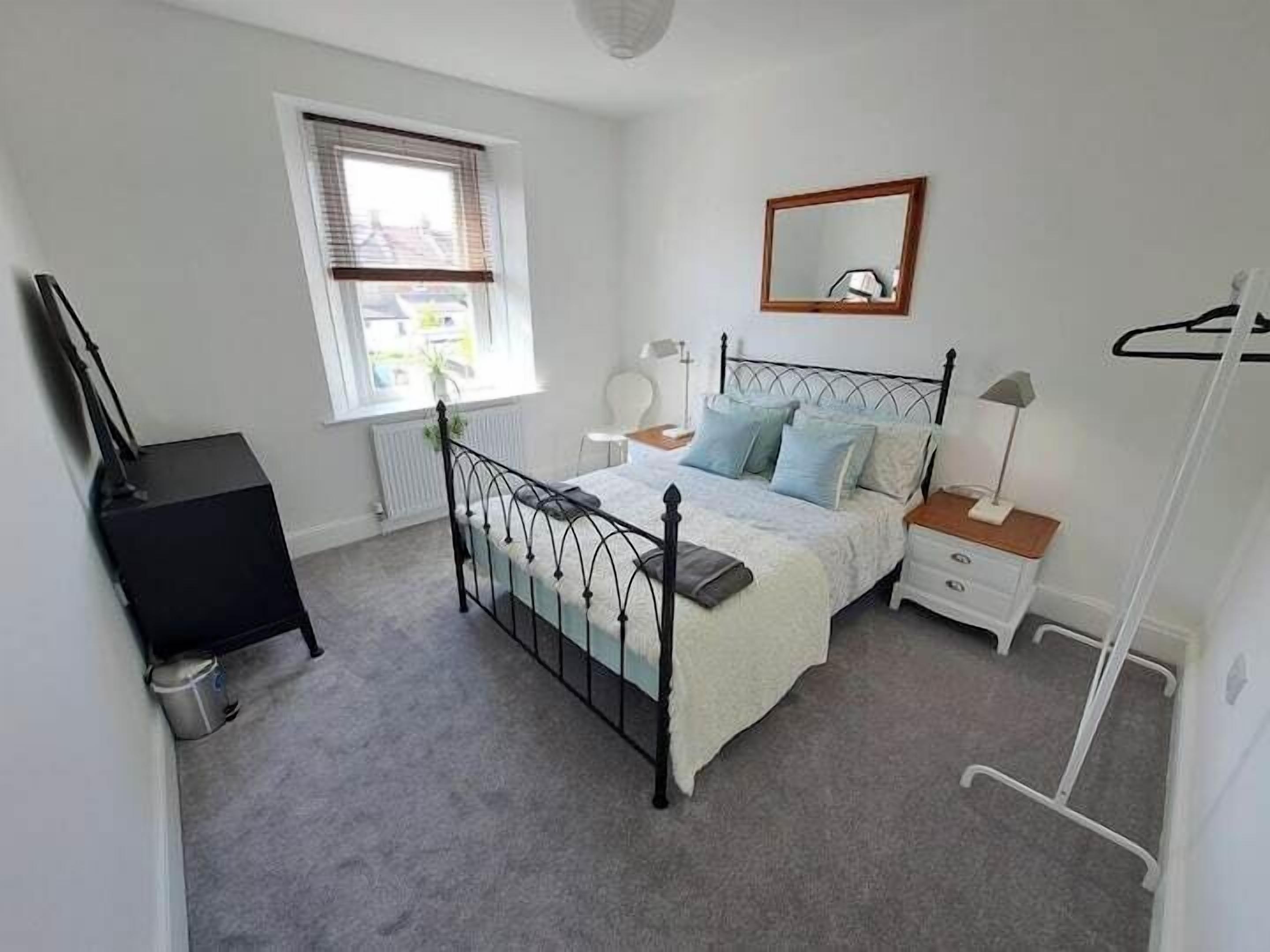 A bedroom with a bed, bedside tables, a dresser, a window, and a radiator.