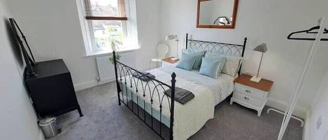 A bedroom with a bed, bedside tables, a dresser, a window, and a radiator.