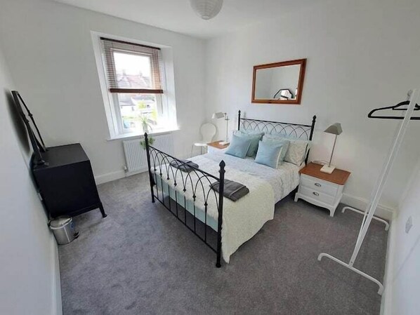 Un dormitorio con cama, mesitas de noche, cómoda, ventana y radiador.