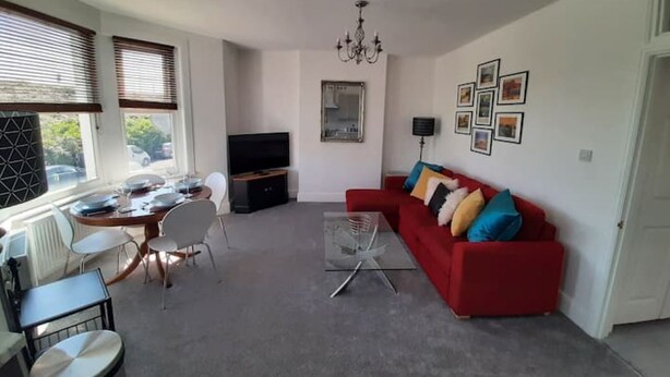 Ein Wohnzimmer mit einem roten Sofa, einem Glastisch, einem Fernseher und einem Essbereich mit Tisch und Stühlen.