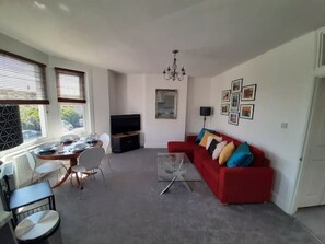 Una sala de estar con un sofá rojo, una mesa de centro de vidrio, un televisor y un comedor con una mesa y sillas.