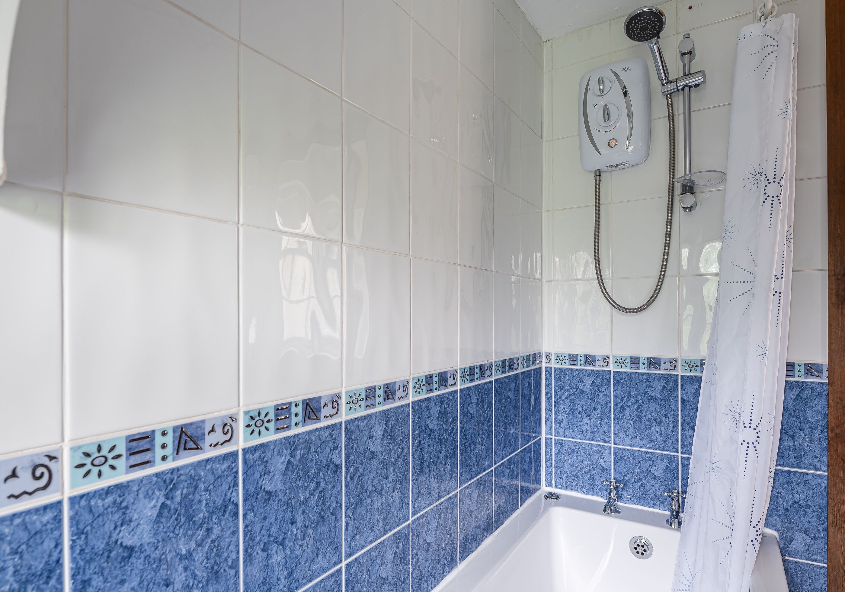 A bathroom with white and blue tiles, a shower, and a bathtub.