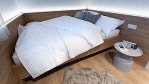 A neatly made bed with white linens, a small bedside table with a book and a cup, and a fluffy rug on the floor.