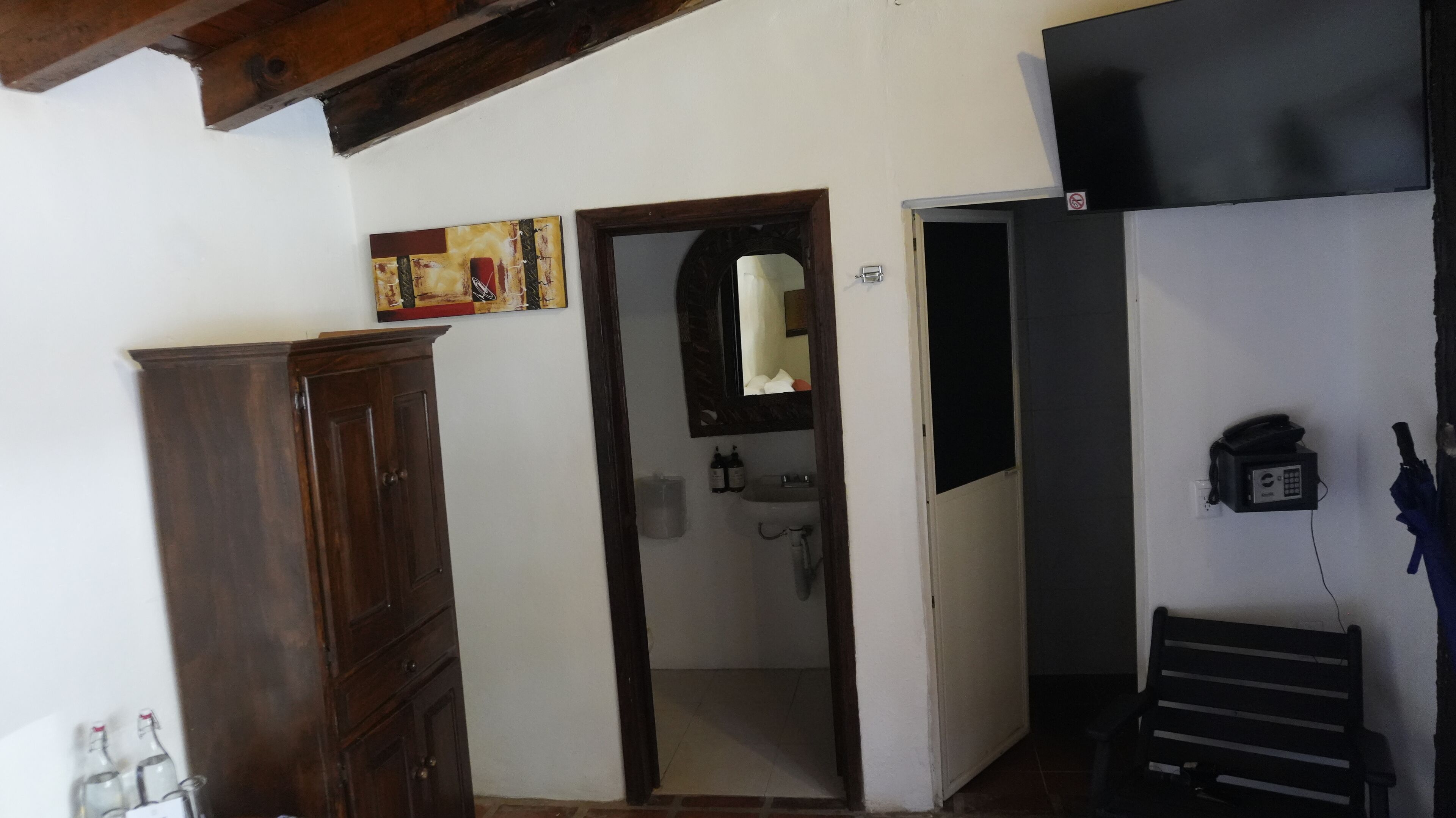 Quarto com guarda-roupa de madeira, banheiro com espelho e pia, e um telefone.