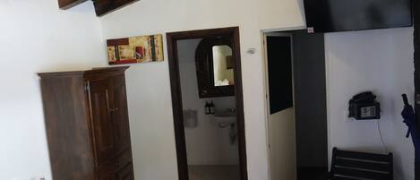 Quarto com guarda-roupa de madeira, banheiro com espelho e pia, e um telefone.