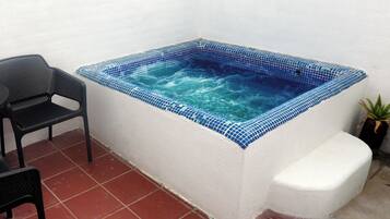 Un jacuzzi rectangular con mosaicos azules, una silla de metal negro y una planta en maceta a su lado.