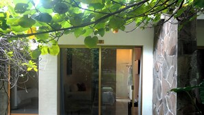 A building entrance with a glass door, a stone wall, and a small garden area with green leaves. - Las Jaras Aguas Termales (Tamazula de Gordiano)