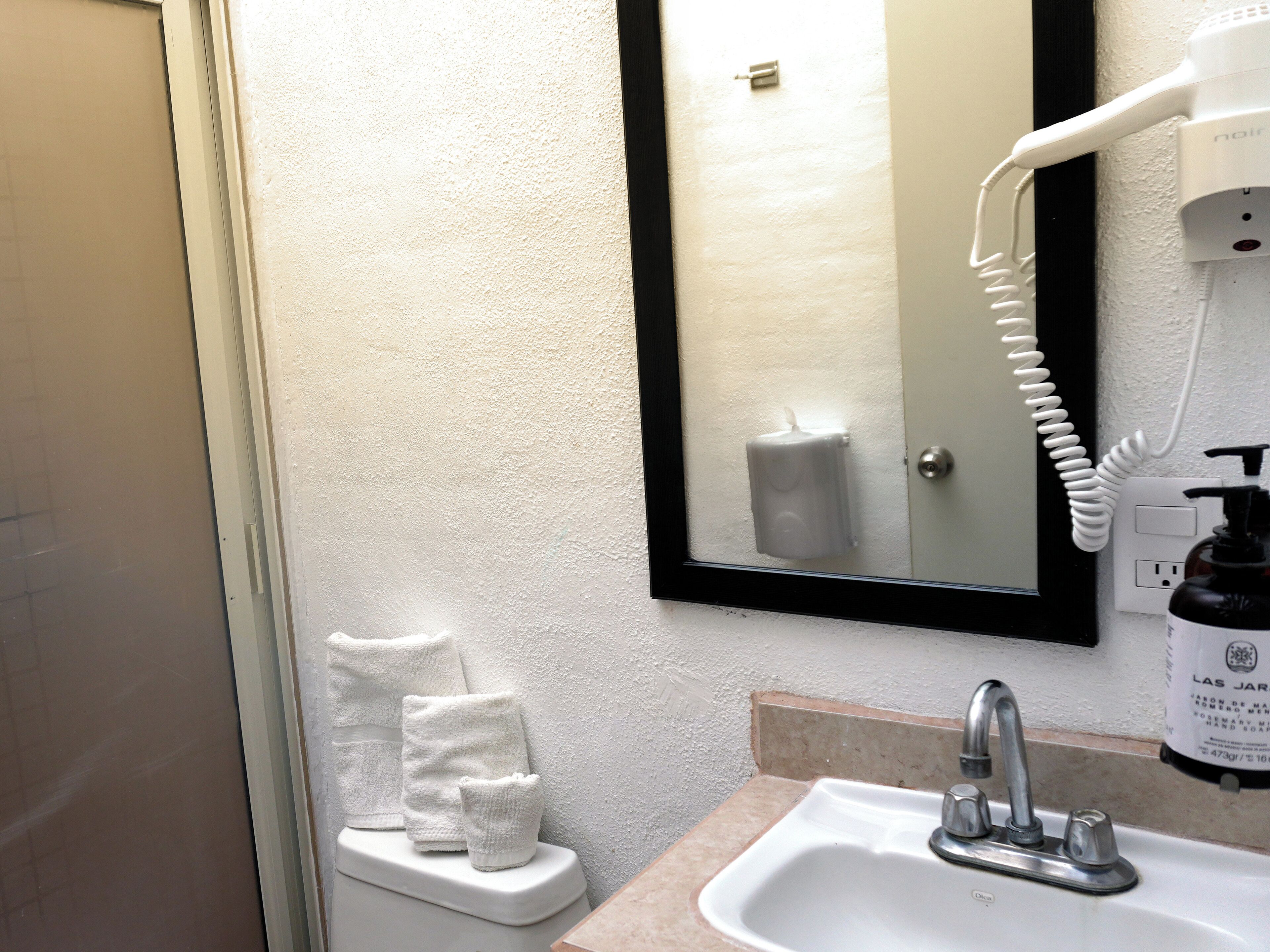 Une salle de bain avec un lavabo blanc, un miroir et un sèche-cheveux fixé au mur.