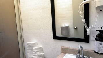 Une salle de bain avec un lavabo blanc, un miroir et un sèche-cheveux fixé au mur.