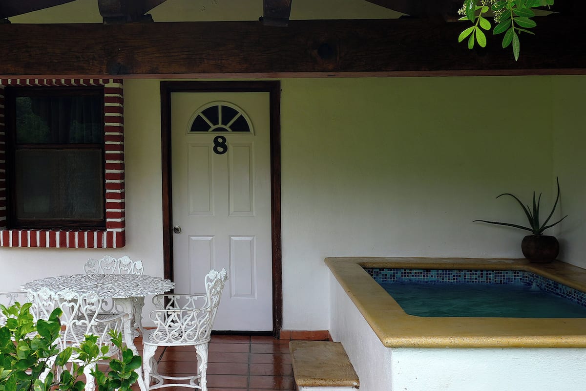 A covered patio area with a white door marked with the number 8, a small pool, and white outdoor furniture.