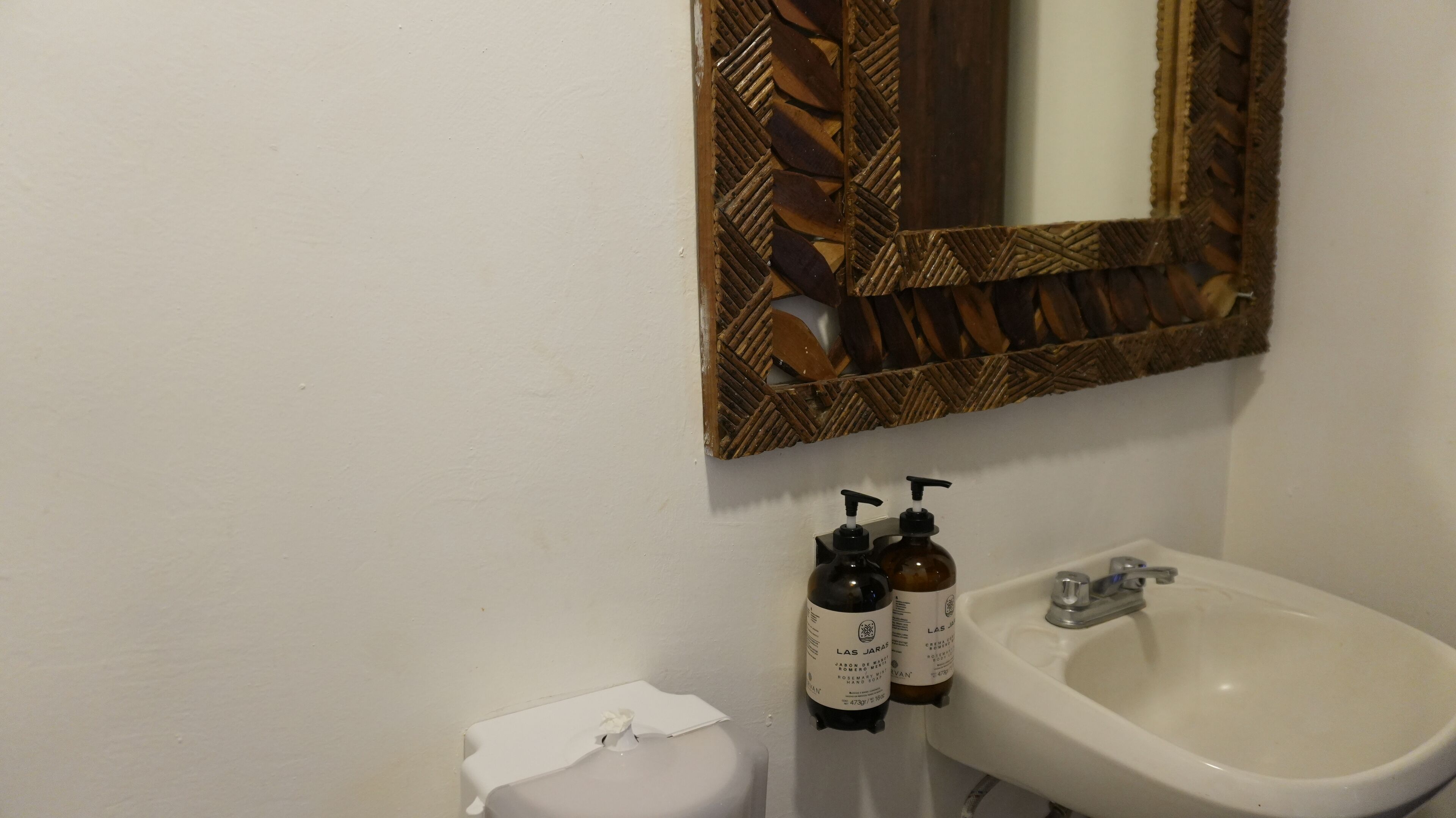 A bathroom with a white sink, a mirror with a wooden frame, and two bottles of hand soap.