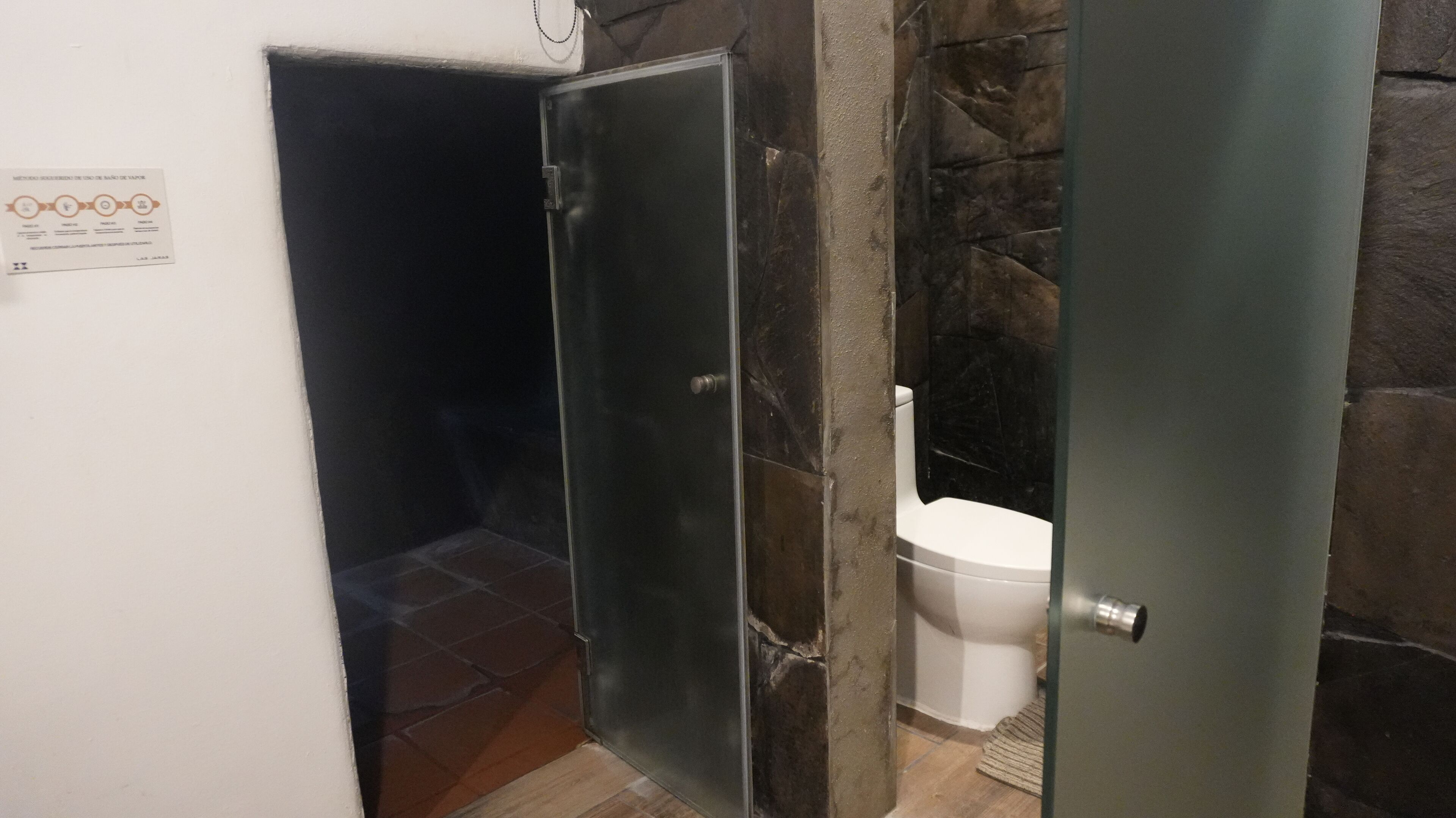 A bathroom with a toilet, a shower area, and a door with a metal handle.