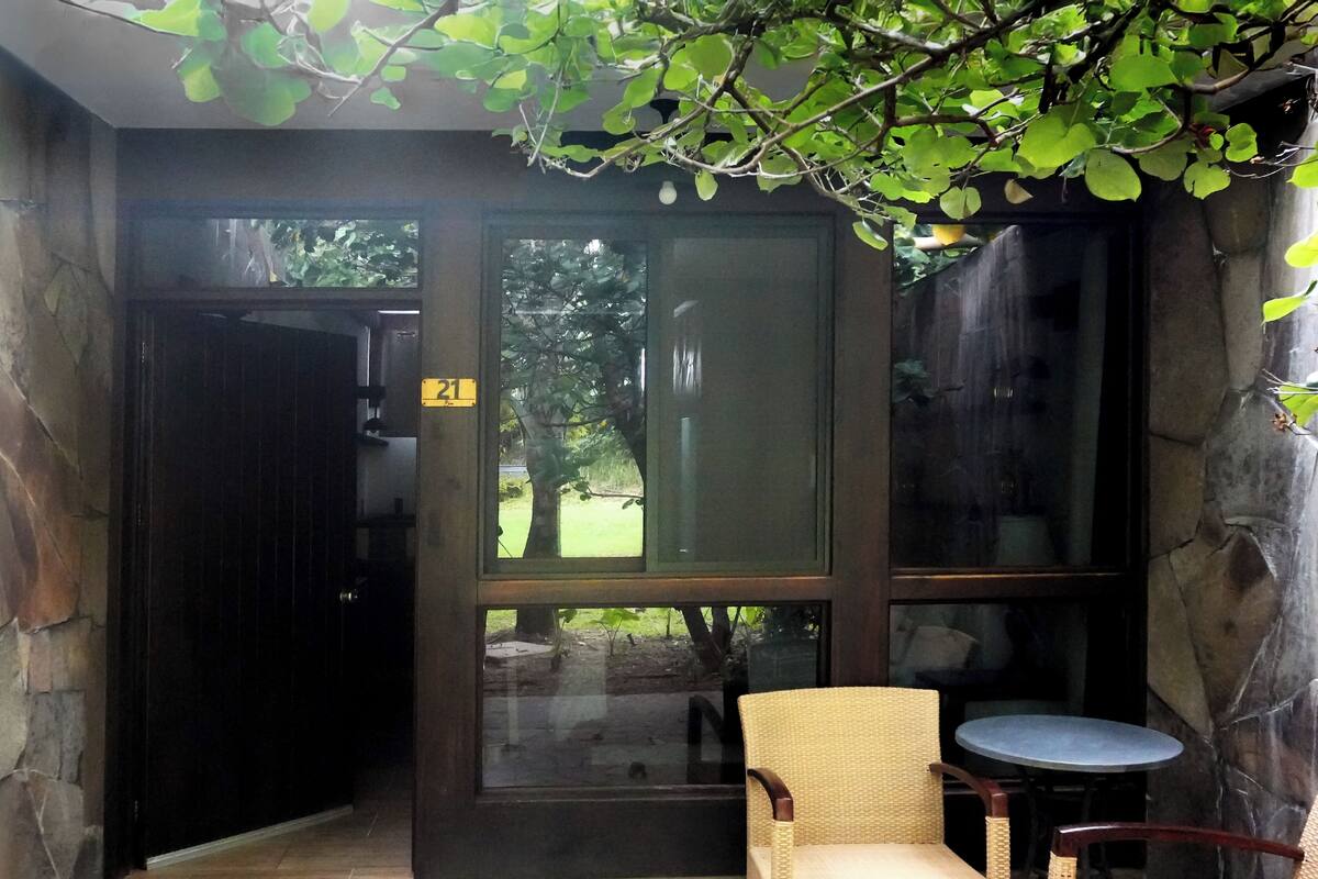 A room with a stone wall, a glass door with the number 21, a wicker chair, and a small round table.