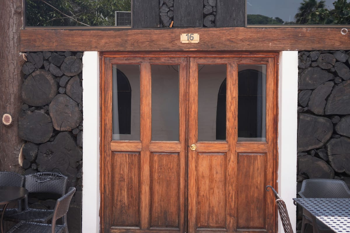 A wooden double door with a number plaque, flanked by stone walls and wicker furniture.