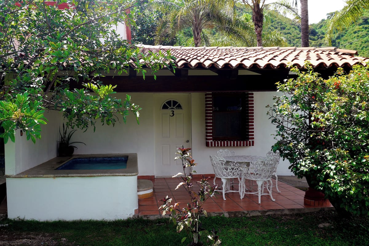 A small house with a tiled roof, a swimming pool, and a patio with a table and chairs.