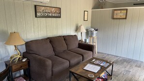 Un salon chaleureux avec un canapé marron, une table basse en bois sur laquelle sont posés des magazines, une lampe et un panneau d’accueil encadré.