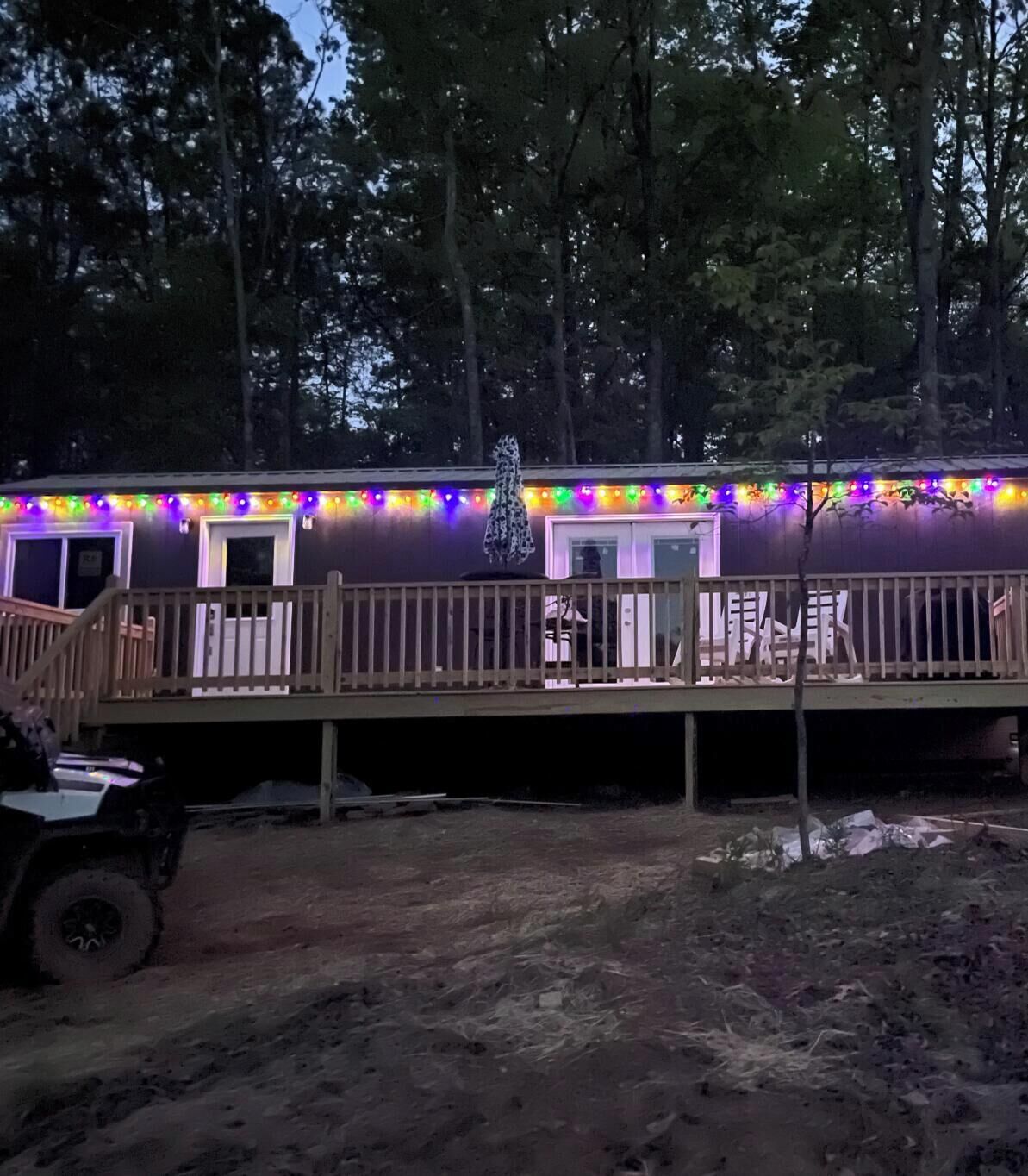 A cabin with a deck, surrounded by trees, and decorated with colorful lights.