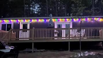 A cabin with a deck, surrounded by trees, and decorated with colorful lights.