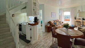 A spacious living area with a staircase leading to a kitchen, a dining table with chairs, and a cozy seating area with a fireplace. - Apt Quatre Saisons (Campos do Jordão)
