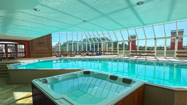 A large indoor swimming pool with a hot tub, wooden flooring, and a glass ceiling. - Apt Quatre Saisons (Campos do Jordão)