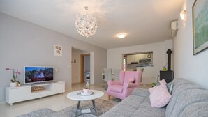 Ein modernes Wohnzimmer mit Fernseher, einem pinkfarbenen Sessel, einem grauen Sofa und einer Chandelieber.