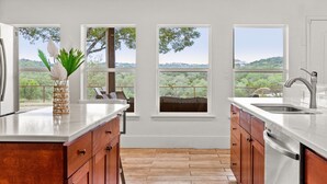 A kitchen with wooden cabinets, a white countertop, and a view of the outdoors through large windows. - Private Hill Country Retreat Near San Antonio (Bexar County)