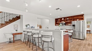 A modern kitchen with a central island, wooden cabinets, stainless steel appliances, and a staircase. - Private Hill Country Retreat Near San Antonio (Bexar County)