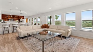 A spacious living area with a large sectional sofa, a glass coffee table, and a kitchen area with bar stools. - Private Hill Country Retreat Near San Antonio (Bexar County)