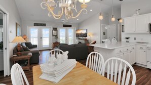 Een ruime woonkamer met een eettafel voor vier personen, een keuken met witte kasten en een grote kroonluchter.