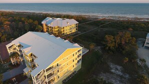 A coastal hotel with multiple buildings, including a large structure with a flat roof and balconies, and a smaller building with a sloped roof. - Dunes Club 1D (Port St. Joe)