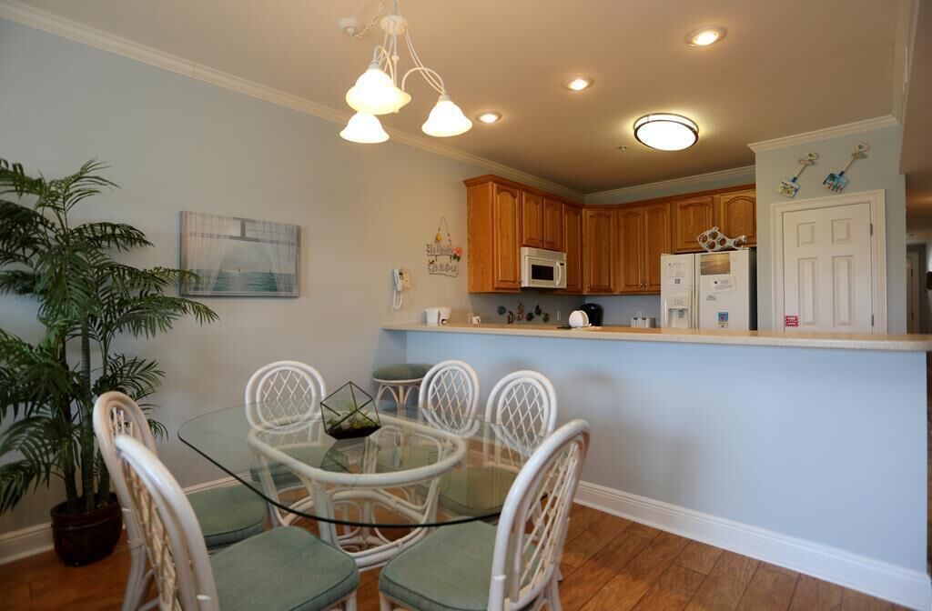 A dining area with a glass table and white chairs, a kitchen with wooden cabinets, and a potted plant.