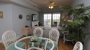 A living room with a ceiling fan, a fireplace, a sofa, and a dining area with white chairs. - Dunes Club 1D (Port St. Joe)